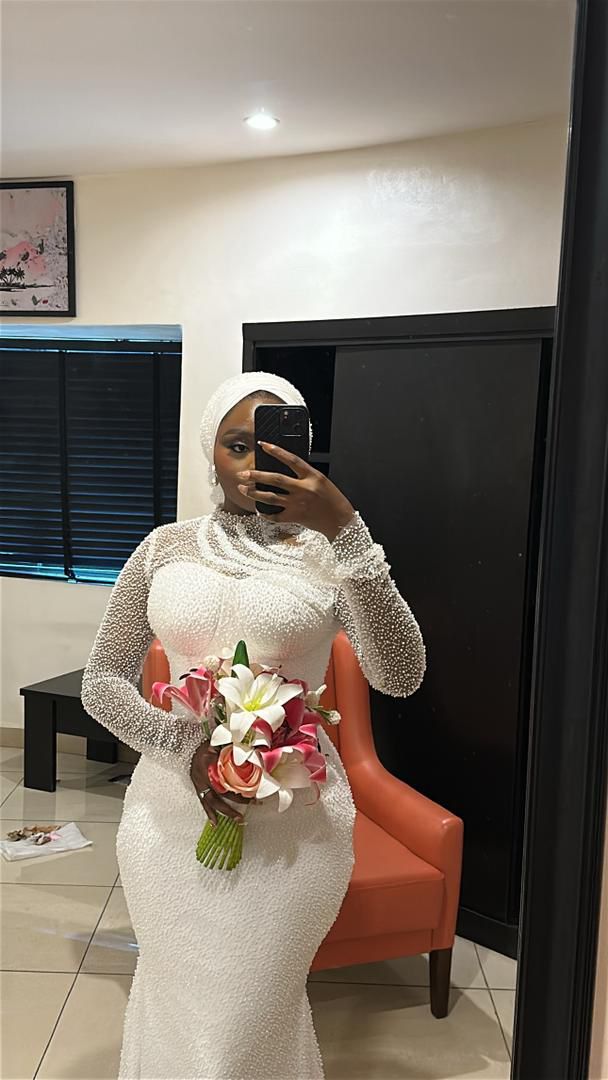 Bride in an ivory pearl-beaded long-sleeve mermaid wedding gown, holding a bouquet.